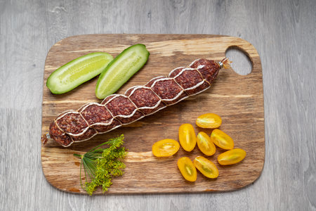 sausage salami with vegetables: cut cucumbers, cherry tomato and dill herb, closeup on the wooden plate, restaurant presentation, nutrition, calories and carbs, high in sodium mealの写真素材