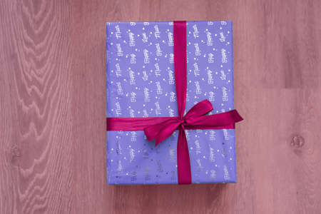 top view of purple violet color gift box with red ribbon bow on light red wooden background. Concept: holiday, celebration, birthday, New Year, Christmas, Valentines Day, Mothersの写真素材