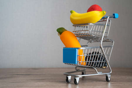 a supermarket cart trolley with fresh vegetables and fruits on a wooden background. Concept of shopping buying healthy foodの写真素材