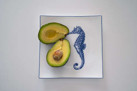 half cut avocado with seed pit, stone, on a white plate with sea horse print, source of vitamins, omega 3 fatty acidsの写真素材