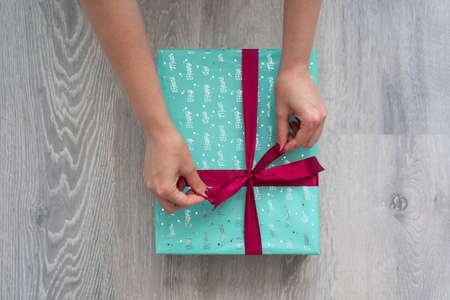 woman hand holding green turquoise color gift box with red ribbon bow on grey wooden background. Concept: holiday, celebration, birthday, New Year, Christmas, Valentines Dayの写真素材