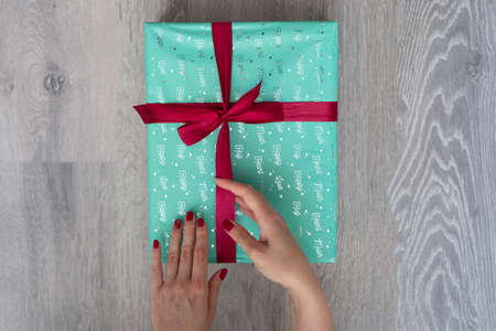 woman hand holding green turquoise color gift box with red ribbon bow on grey wooden background. Concept: holiday, celebration, birthday, New Year, Christmas, Valentines Dayの写真素材