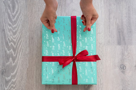 woman hand holding green turquoise color gift box with red ribbon bow on grey wooden background. Concept: holiday, celebration, birthday, New Year, Christmas, Valentines Dayの写真素材
