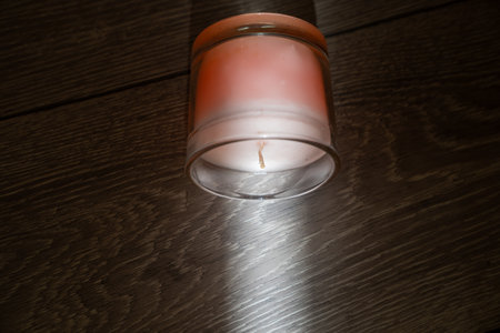 pink scented candle in a glass cover on a wooden background, sunbeam light creates creative effect of burning candle, therapy, meditation, aromatherapy to relax mindsetの写真素材
