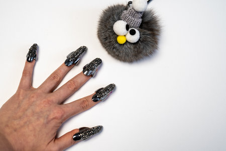 Halloween theme, witch nails, beautiful female hand with stylish manicure and jewellery, nail rings, decoration, magic, spooky, white background, plush toy monster with eyesの写真素材