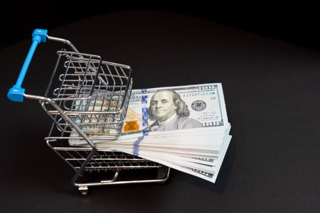 shopping cart trolley with money, pack of hundred dollar bills on black background, concept of buying, money spending, black Friday sale, currencyの写真素材