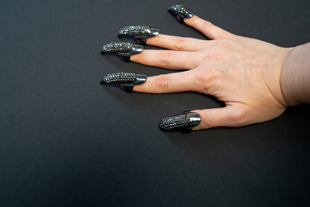 Halloween theme, witch nails, beautiful female hand with stylish manicure and jewellery, nail rings, decoration, magic, spooky, black backgroundの写真素材