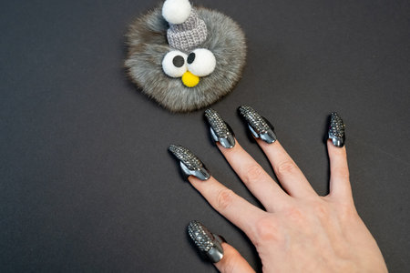Halloween theme, witch nails, beautiful female hand with stylish manicure and jewellery, nail rings, decoration, magic, spooky, black background, plush toy monster with eyesの写真素材