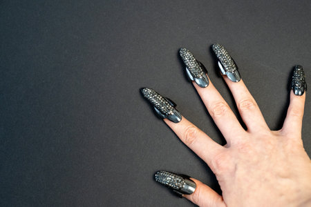 Halloween theme, witch nails, beautiful female hand with stylish manicure and jewellery, nail rings, decoration, magic, spooky, black backgroundの写真素材