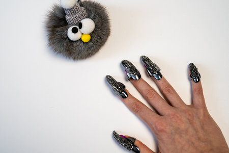 Halloween theme, witch nails, beautiful female hand with stylish manicure and jewellery, nail rings, decoration, magic, spooky, white background, plush toy monster with eyesの写真素材
