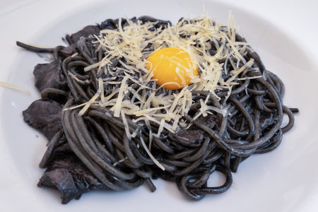 dark spaghetti pasta with egg and cheese on a white plate at restaurant, eating out, way of serving food, cookingの写真素材