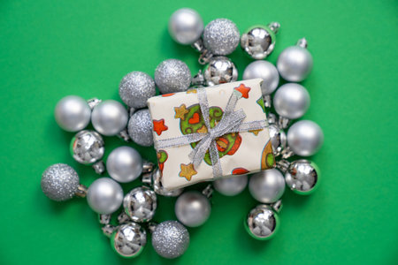 wrapped gift box with christmas, new year print decorations and tied bow, surrounded by silver balls baubles on green background, festive holidays time, copy spaceの写真素材