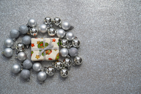 gift box with christmas, new year print decorations and tied bow, surrounded by silver balls baubles on grey sparkle background, festive holidays timeの写真素材