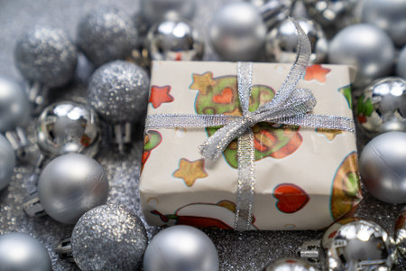 gift box with christmas, new year print decorations and tied bow, surrounded by silver balls baubles on grey sparkle background, festive holidays timeの写真素材