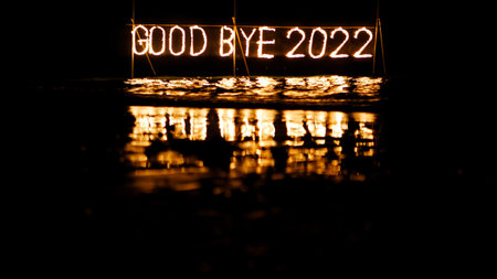 good bye 2022 burning phrase made of fire stick placed on water in sea, happy new year celebration in tropical place at night, inscription on the beachの写真素材