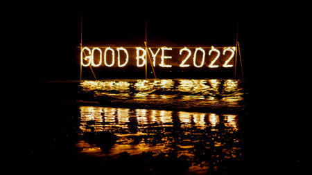 good bye 2022 burning phrase made of fire stick placed on water in sea, happy new year celebration in tropical place at night, inscription on the beach, reflectionの写真素材