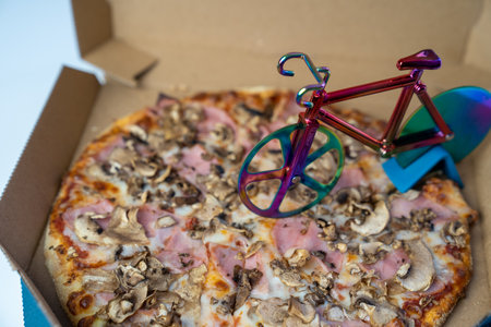 blur effect, delicious pizza in carton box on table, bicycle pizza cutter knife on cheese in cardboard, fast food delivery serviceの写真素材