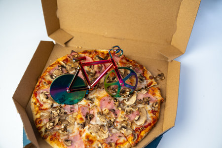 blur effect, delicious pizza in carton box on table, bicycle pizza cutter knife on cheese in cardboard, fast food delivery serviceの写真素材
