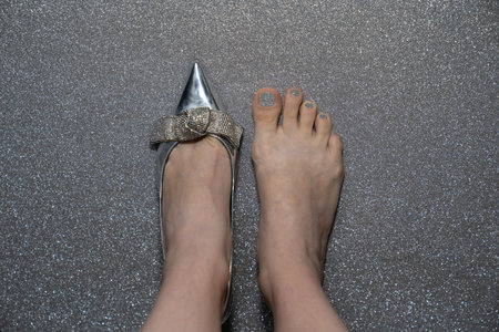 female feet with silver fashion shoe, woman wears heels on one leg, second leg barefoot with pedicure, concept of trying shoes in the storeの写真素材