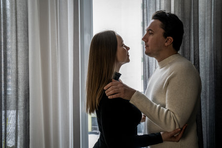 romantic couple hugging each other near window at home, woman in black man in white, yin yang contrast, opposites attract. Love my second halfの写真素材