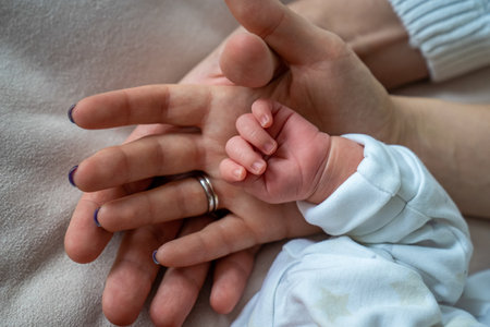 father and mother holding newborn baby's hand, close up family hold hands together, parent's love, tiny little fingers, happiness and careの写真素材
