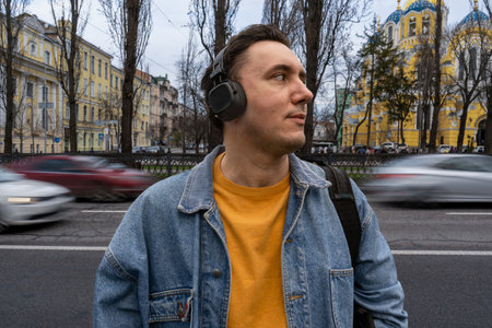 handsome black haired man in blue jeans jacket is standing on the street near heavy traffic. Person...