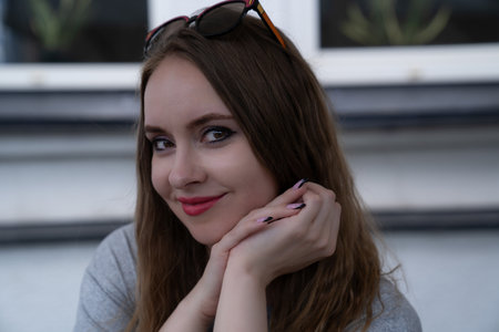 young pretty woman with good skin, beautiful big brown eyes, natural hair color, red lips, sitting in the street and smiling. Girl portrait. Looking at the camera, visible handsの写真素材