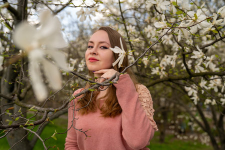beautiful blond natural hair woman in pink outfit is posing in botanical garden park near blooming magnolia tree with flowers. Spring and purity, natural beauty. Woman Dayの写真素材