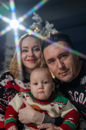 Happy family Christmas portrait featuring mother, father, and baby in festive holiday sweaters. The...