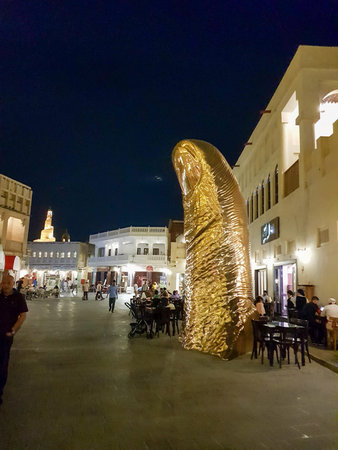 Doha, Qatar - March 26 2026: Close-up of golden thumb sculpture at Souq Waqif surrounded by visitors...