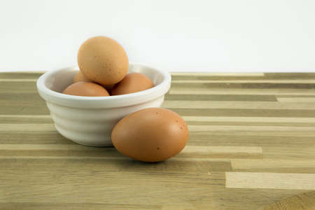 Free range eggs in a white bowl on oak worktop.
