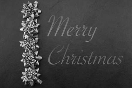 Pewtersilver bows and merry christmas on a slate backgroundの写真素材