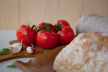 Fresh tomatoes on wooden desk with garlic and loaf of bread. Organic food.の写真素材