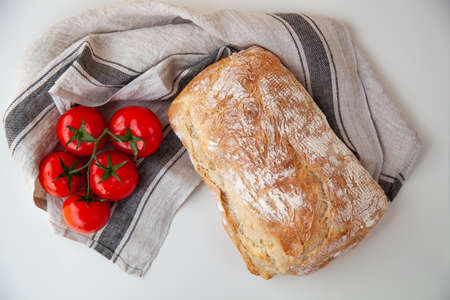 Loaf of fresh bread on the table on textile napkin with tomatoes. Organic food.