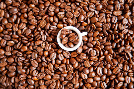 A small white cup of coffee stands on coffee beans. Top view.