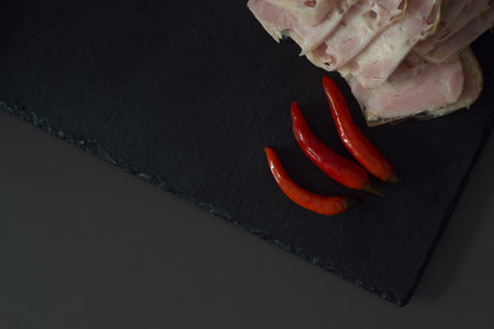 Slices of ham and chilli pepper on black slate plate