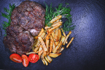 Grilled beefsteak with french fries and vegetables on black backgroundの写真素材