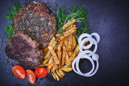 grilled beefsteak with fries and vegetables on a black backgroundの写真素材
