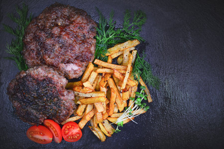 Grilled beef cutlets with french fries and vegetables on black backgroundの写真素材