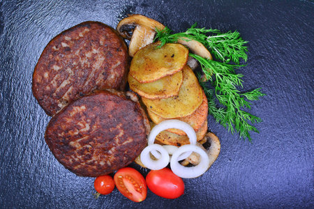 Grilled hamburger with fried potatoes and vegetables on a black backgroundの写真素材