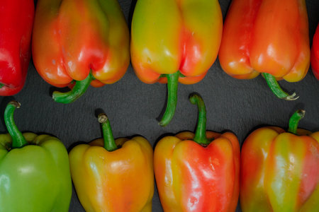 Red, green and yellow bell peppers on black slate background. Top view.