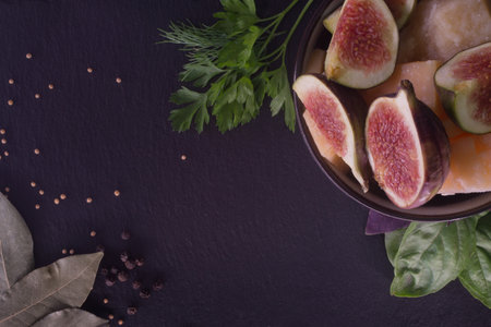 Fresh figs and cheese with herbs and spices on black slate background