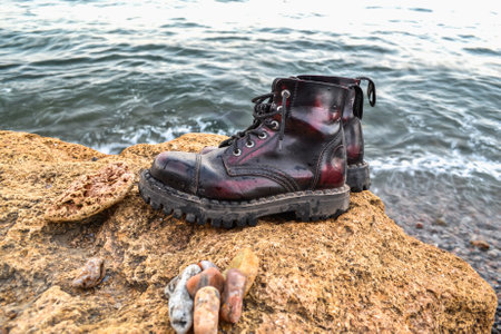Pair of black hiking boots on a rock near the sea.