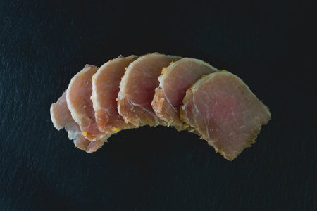 Slices of ham on a black background. Toned.