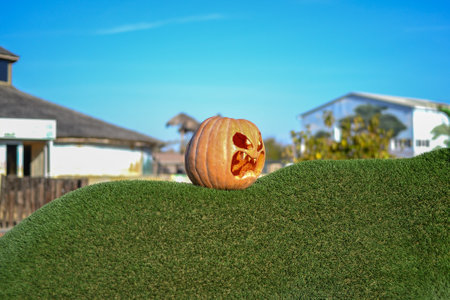 Halloween pumpkin on green grass in front of house with blue skyの写真素材