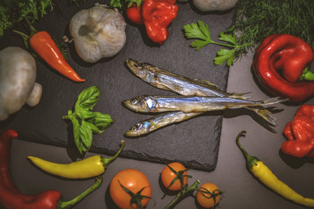 Fresh raw sardines with herbs and vegetables on black stone backgroundの写真素材