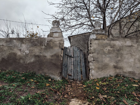 Old stone wall with a gate and an entrance to an abandoned houseの写真素材