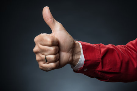 Man showing thumbs up gesture on dark background. Selective focus.の素材