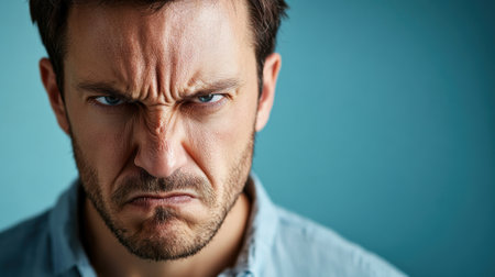 Close-up portrait of an angry man with a furrowed brow and intense expression, glaring directly at the camera against a plain background.の素材