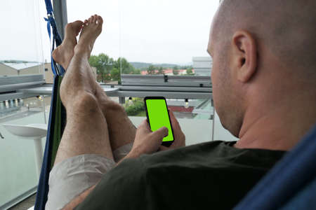 male lying on a hammock with cellphone with green screenの写真素材